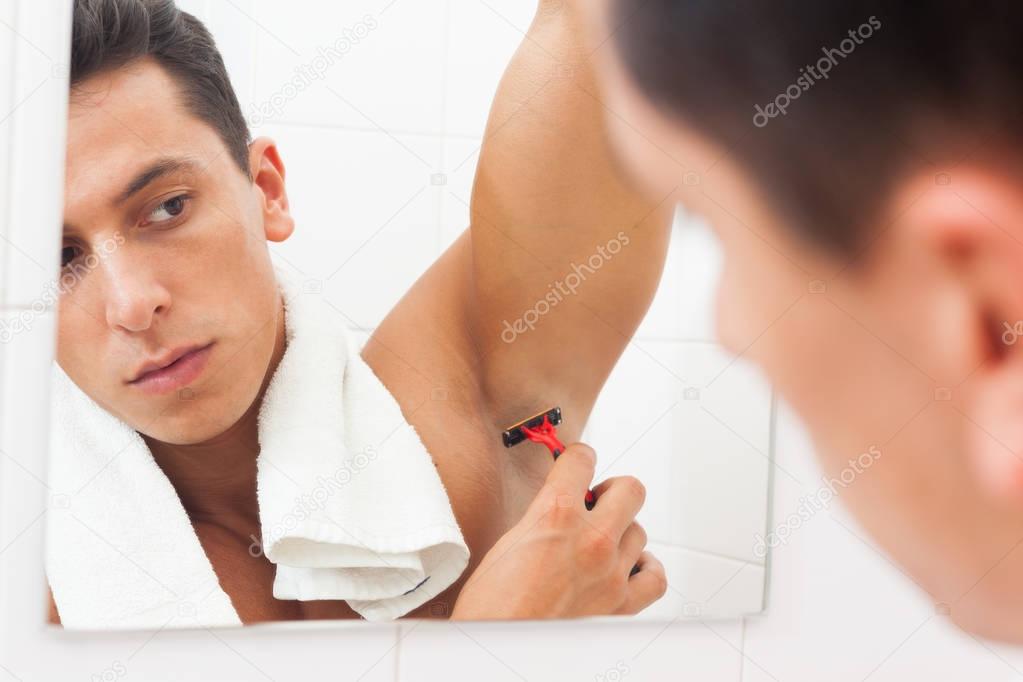 Young man using razor to remove hair from his armpit