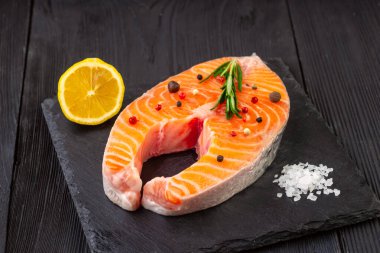 Siyah arka planda tuzlu, baharatlı ve biberiyeli çiğ somon balığı bifteği..