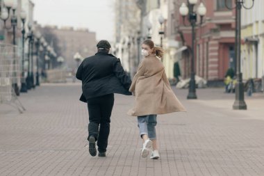 Birbirine aşık bir çift, kadın ve erkek, yüzünde koruyucu maskeyle boş caddede yürür. Çevre kirliliği kavramı. Guy, kız Çin salgınına karşı koronavirüs, virüs koruması