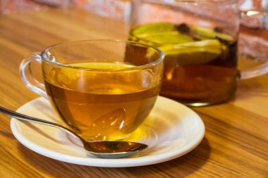 Temiz bardakta sıcak çay ve ahşap masa arkasında çaydanlıkta çay... Sağlıklı çay konsepti