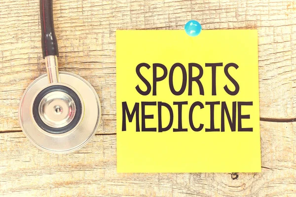 Sports medicine text on yellow paper with stethoscope on wooden background