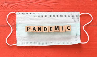 Pandemikti. Pandemik kelimesi, koruyucu bir maske ve kırmızı bir masa üzerindeki ahşap harflerden düzenlenmiştir..