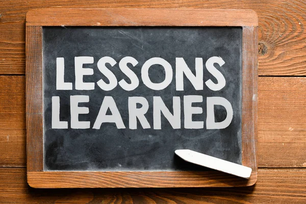 LESSONS LEARNED words written on a chalk board located on a wooden table.
