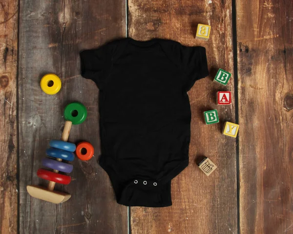 黑色婴儿紧身衣裤的样机平躺在褐色质朴的木材背景上的玩具 — 图库照片