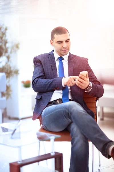 Jovem empresário bem sucedido digitando sms no telefone no local de trabalho — Fotografia de Stock
