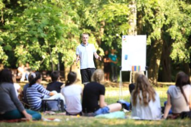 Bir grup genç öğrenci parkta. Ufuk bir grup insan önünde çim üzerinde oturan karşı ayakta elleriyle gesticulating bir adam görünümü.