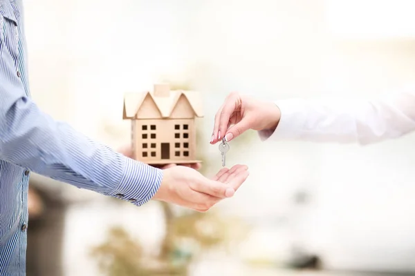 Mann übergibt einer Frau einen Hausschlüssel mit Schlüsselanhänger in der Form seines Hauses. — Stockfoto