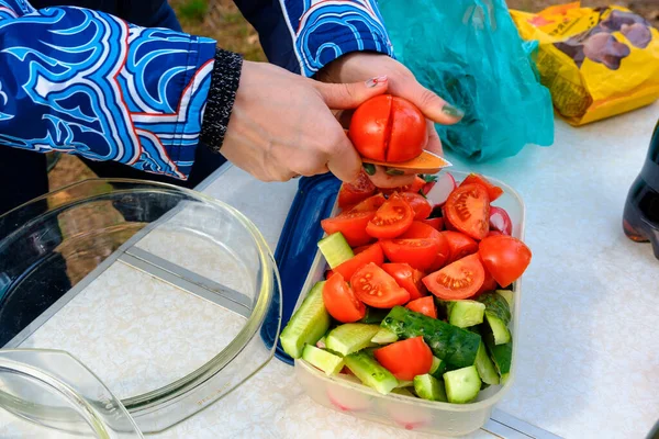 Woman cuts tomato and cucumber salad on outdoor — Stock Photo, Image