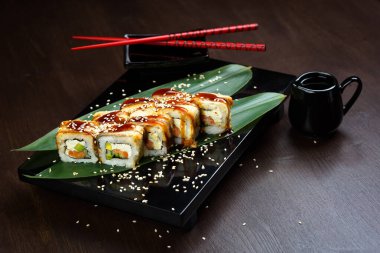 Sosu ve kırmızı çubuğu olan tahtanın üzerinde yılan balığı ve peynirli rulo.