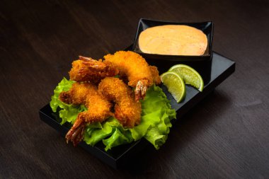 Kızarmış karides soslu, salata yapraklı ve limonlu kara tahtada.