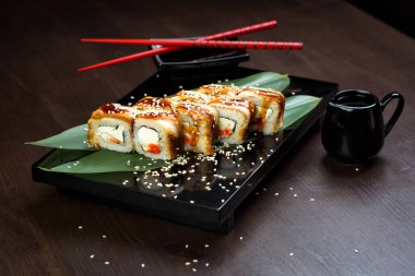 Sosu ve kırmızı çubuğu olan tahtanın üzerinde yılan balığı ve peynirli rulo.