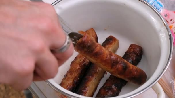 Un hombre saca las salchichas del pincho en un plato de vidrio. Cocinar al aire libre — Vídeo de stock