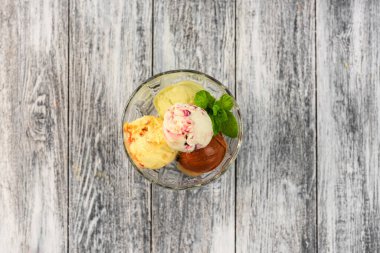 Ahşap arka planda, camda duran renkli dondurma topları.