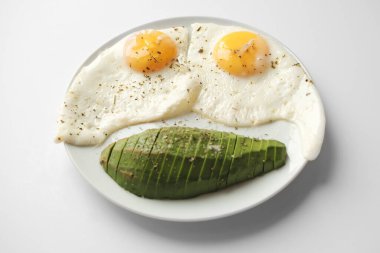 Avokado ile çırpılmış yumurta ve özellikle beyaz arka planda beyaz bir tabakta. Yakın çekim, üst görünüm