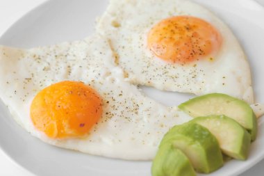 Avokado ile çırpılmış yumurta ve özellikle beyaz arka planda beyaz bir tabakta. Yakın çekim, üst görünüm