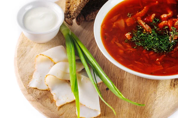 Borscht with sour cream, green onions, bacon and rye bread on a round wooden Board on white background, view closeup — Stock Photo, Image