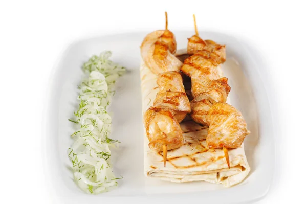 Shish kebab på ett spett med lavash, lök och grönt på en vit platta på vit isolerad bakgrund — Stockfoto