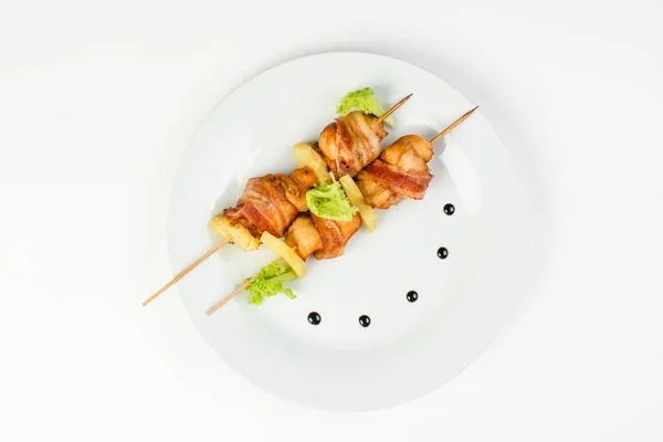 Brochettes de poulet et d'ananas avec bacon sur une assiette ronde blanche sur fond blanc isolé Photos De Stock Libres De Droits