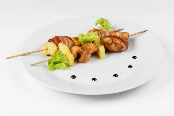 Brochettes de poulet et d'ananas avec bacon sur une assiette ronde blanche sur fond blanc isolé Images De Stock Libres De Droits