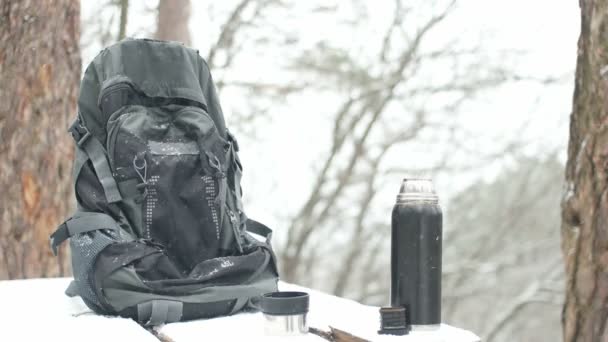 Mochila e uma garrafa térmica e queda de neve — Vídeo de Stock