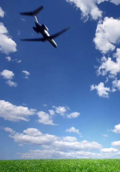 Самолет летит в голубом небе над зеленым грассом — стоковое фото