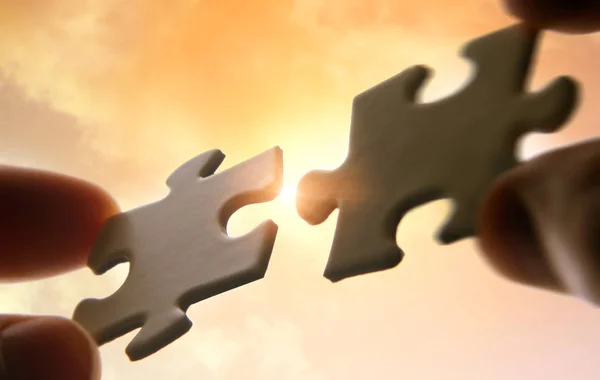 Putting puzzle pieces together on sky background with sunlight — Stock Photo, Image