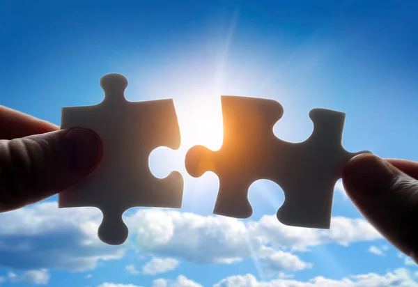 Putting puzzle pieces together on sky background with sunlight — Stock Photo, Image