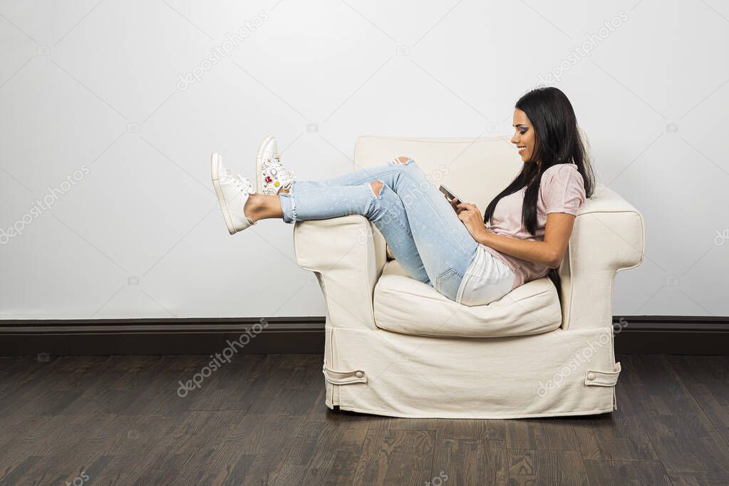 Young woman with her leg up on the arm of the chair, looking at her phone