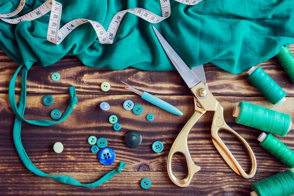 Sewing tools, green fabric, threads and buttons on a wooden background — Stock Photo, Image