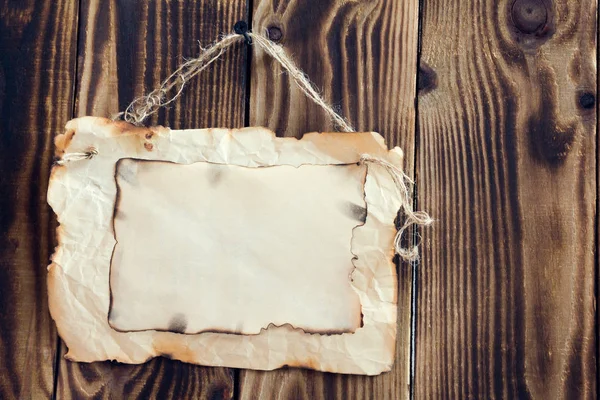Hanging scorched paper on a wooden background — Stock Photo, Image