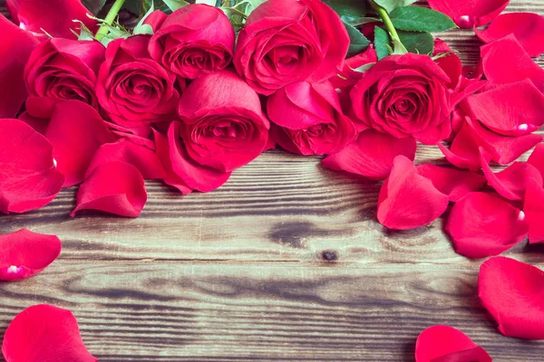 Red roses in a bouquet and the scattered petals on a wooden back — Stock Photo, Image