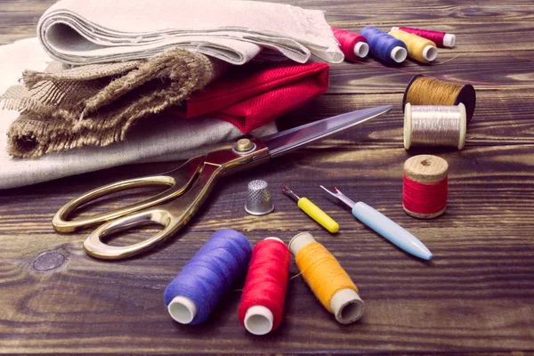 Sewing tools, multi-coloured fabric and threads on a wooden background — Stock Photo, Image