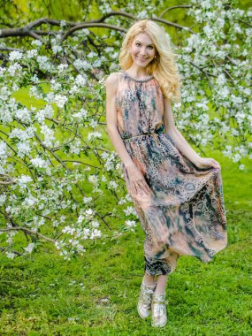 güzel Rus kız sarışın uzun yaz elbise yeni gelişen bir elma ağacı arka planı