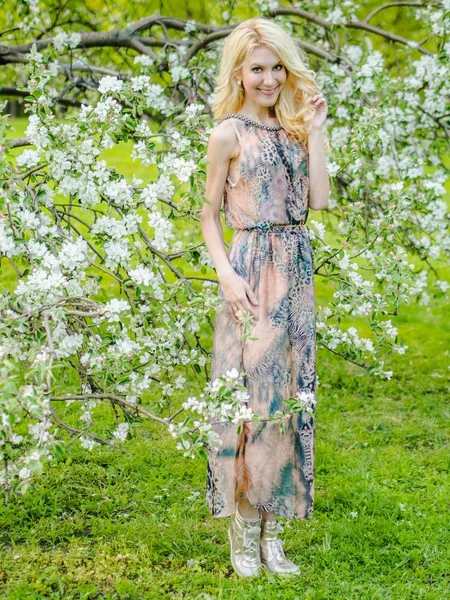 Mooi Russisch meisje Blond in een lange zomerjurk tegen de achtergrond van een bloeiende appelboom — Stockfoto