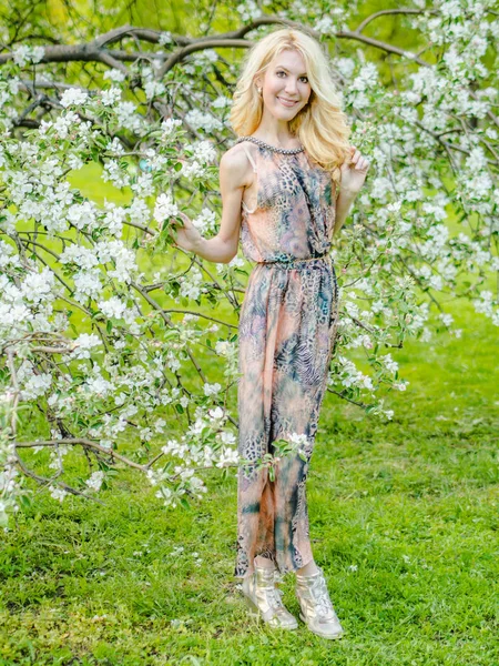 Mooi Russisch meisje Blond in een lange zomerjurk tegen de achtergrond van een bloeiende appelboom — Stockfoto