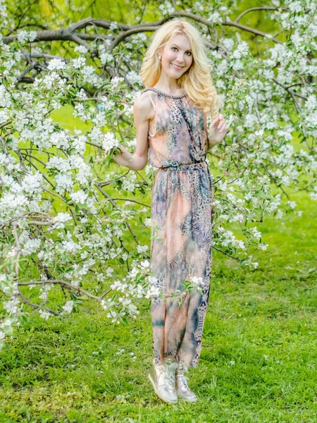 Mooi Russisch meisje Blond in een lange zomerjurk tegen de achtergrond van een bloeiende appelboom — Stockfoto