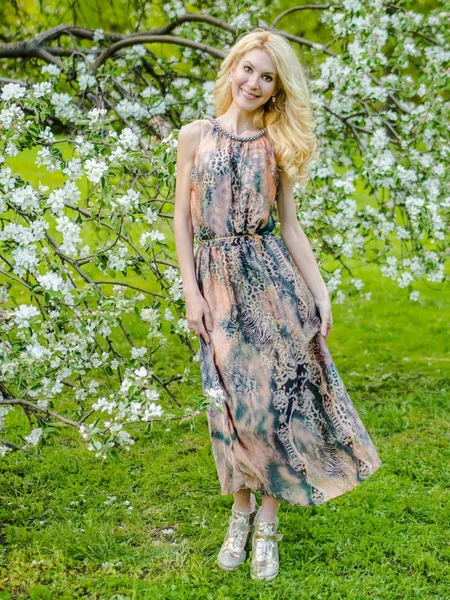 Mooi Russisch meisje Blond in een lange zomerjurk tegen de achtergrond van een bloeiende appelboom — Stockfoto