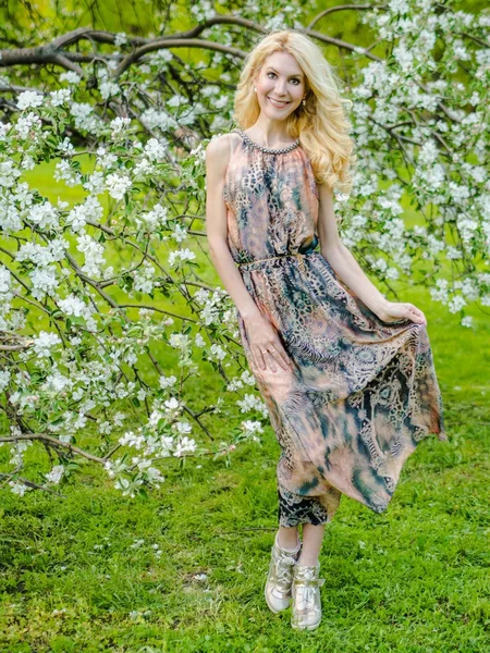 Mooi Russisch meisje Blond in een lange zomerjurk tegen de achtergrond van een bloeiende appelboom — Stockfoto