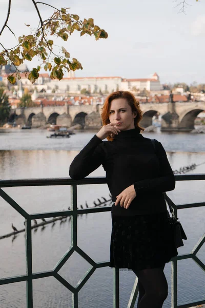 Šťastný rusovlasý turistický cestovatel v Praze, Česká republika v černém svetru s Karlovým mostem v pozadí — Stock fotografie