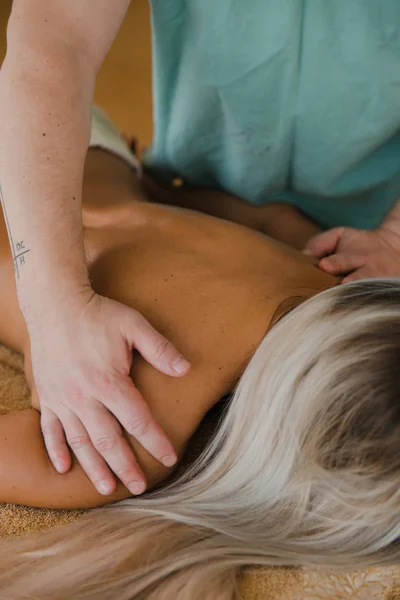Blonde woman relaxing receiving back massage from male physiotherapist in beauty salon lying on massage table. Young girl with tattoos relaxing in spa center concept - Close-up