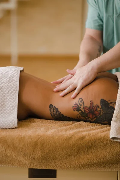 Mujer rubia relajante recibiendo masaje de espalda de fisioterapeuta masculino en el salón de belleza acostado en la mesa de masaje. Chica joven con tatuajes relajante en concepto de centro de spa - Medio — Foto de Stock