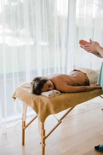 Mujer rubia relajante recibiendo masaje de espalda de fisioterapeuta masculino en el salón de belleza acostado en la mesa de masaje. Chica joven con tatuajes relajante en concepto de centro de spa - Primer plano — Foto de Stock