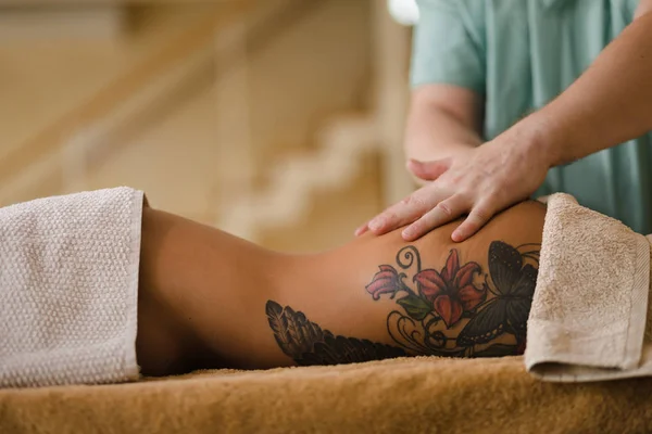 Blond vrouw ontspannen ontvangen rugmassage van mannelijke fysiotherapeut in schoonheidssalon liggend op massagetafel. Jong meisje met tatoeages ontspannen in spa center concept - Medium — Stockfoto