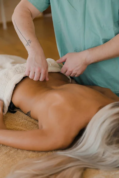 Blondynka relaksująca się otrzymująca masaż pleców od fizjoterapeuty w salonie piękności leżącego na stole do masażu. Młoda dziewczyna z tatuażami relaks w centrum spa koncepcja - Close-up — Zdjęcie stockowe