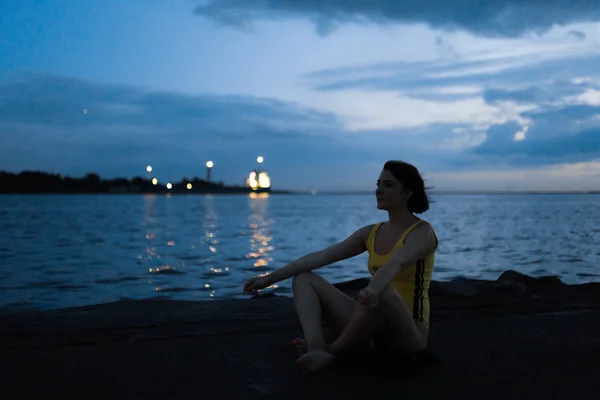 Meditación de cuerpo amarillo: Joven morena por la noche en un lugar donde el río se encuentra con el mar en el puerto —  Fotos de Stock