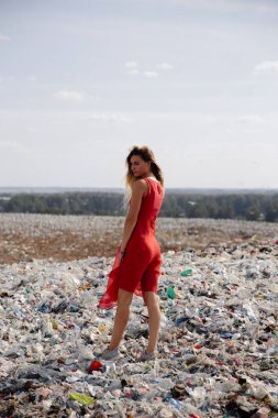 Doğayı kirletme eylemcisi, dışarıdaki büyük bir çöplükte kırmızı elbiseli genç sarışın kadın dünyamızdaki tüm insan atıklarına ve plastiklerine bakıyor Doğu Avrupa 'da Letonya Riga' da uçan martılar
