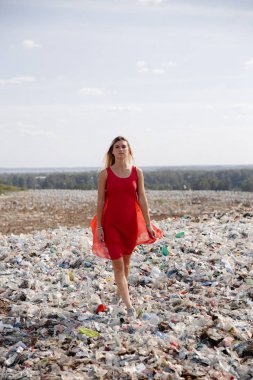 Doğayı kirletme eylemcisi, dışarıdaki büyük bir çöplükte kırmızı elbiseli genç sarışın kadın dünyamızdaki tüm insan atıklarına ve plastiklerine bakıyor Doğu Avrupa 'da Letonya Riga' da uçan martılar