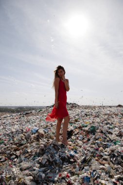 Doğayı kirletme eylemcisi, dışarıdaki büyük bir çöplükte kırmızı elbiseli genç sarışın kadın dünyamızdaki tüm insan atıklarına ve plastiklerine bakıyor Doğu Avrupa 'da Letonya Riga' da uçan martılar