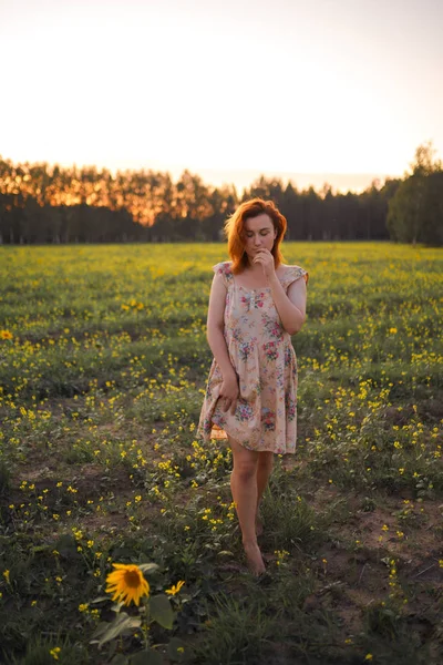 Beautiful redhead woman in a summer short dress during Golden Hour in a sunflower field in Eastern Europe Latvia Smarde