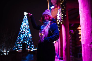 Noel ağacı yıldızına dokunmak - Genç çekici kızıl saçlı kız lunaparkta takılıyor parlak renkli çekimler ve kurulum geçmişiyle